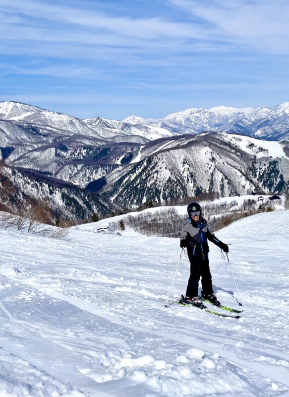 Skier in foregraound at Happo One resort in Japan, with Japanese Alps in background.