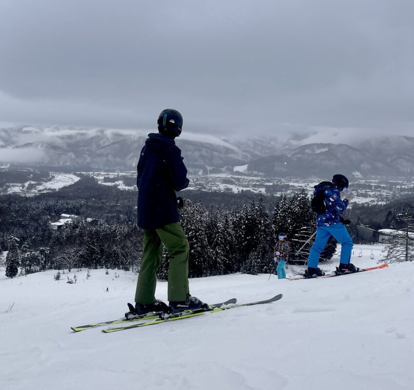 Skier looking out across Hakuba ski resort Happo One with second skier in blue pants in foreground.