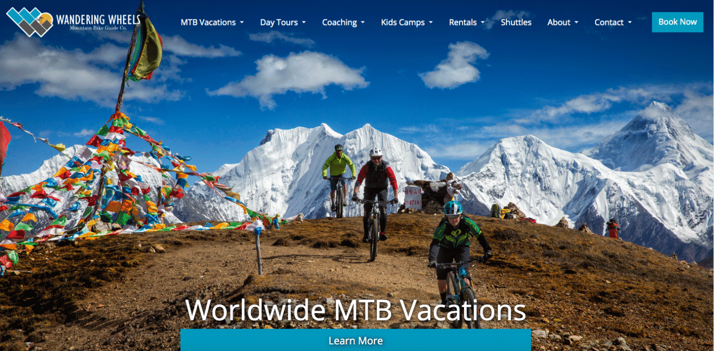 Screenshot of home page of Wandering Wheels mountain bike tour operator with mtb riders and Himilayan prayer flags in foreground and Nepalese mountain range in background.